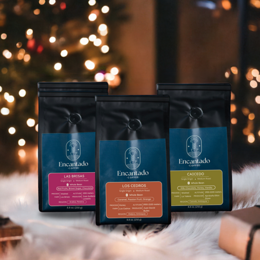 3 coffee bags with dark blue labels sit on a white shag rug in front of a Christmas tree with warm white lights.