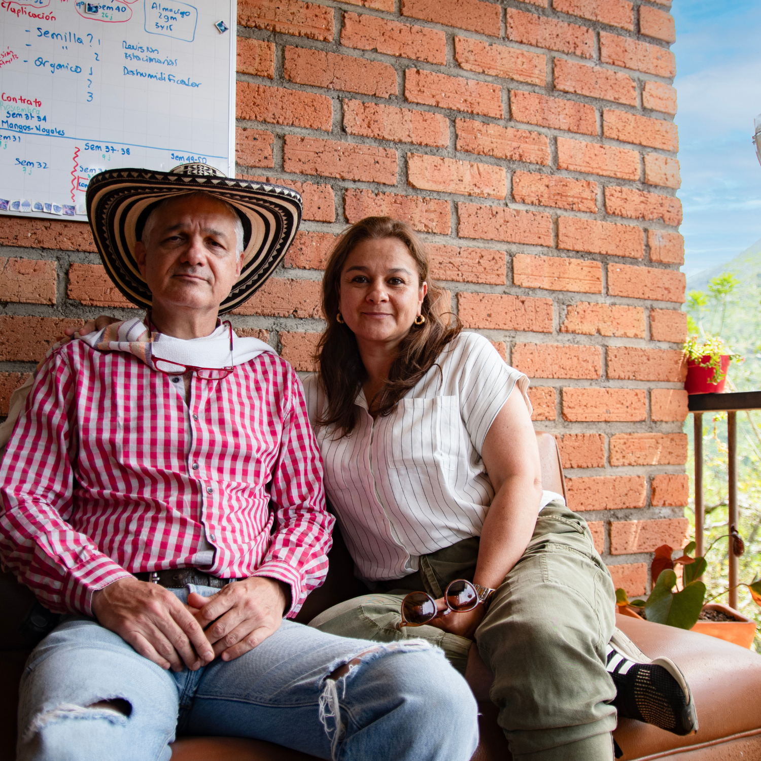 Samuel and Paula sitting on a sofa with a red brick wall in the background