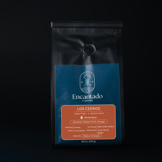 A black bag of Los Cedros Coffee with an orange and blue label sits in front of a black background.